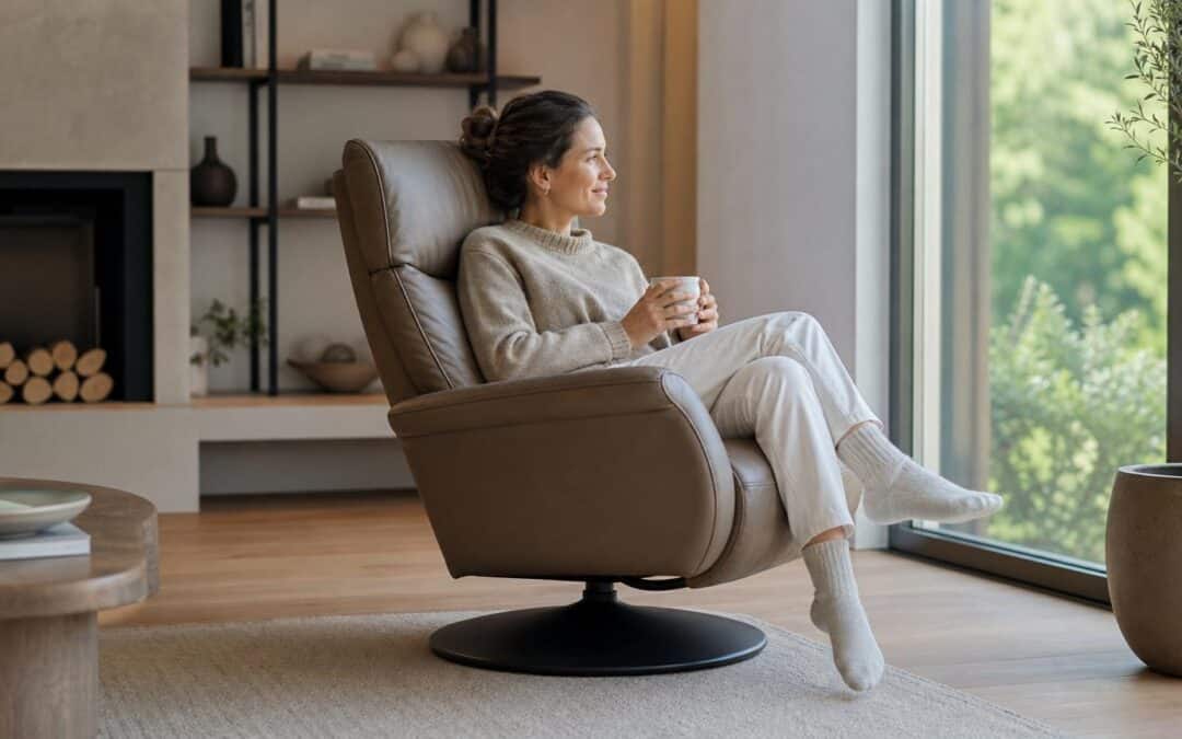 Woman relaxing in a brown leather swivel recliner chair with a mug, looking out a large window in a modern living room.