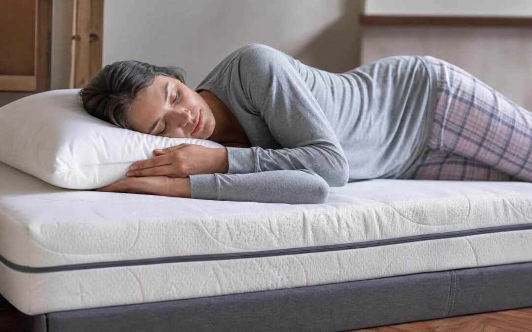 Woman sleeping peacefully on her side on a firm white mattress with a grey base and white pillow.